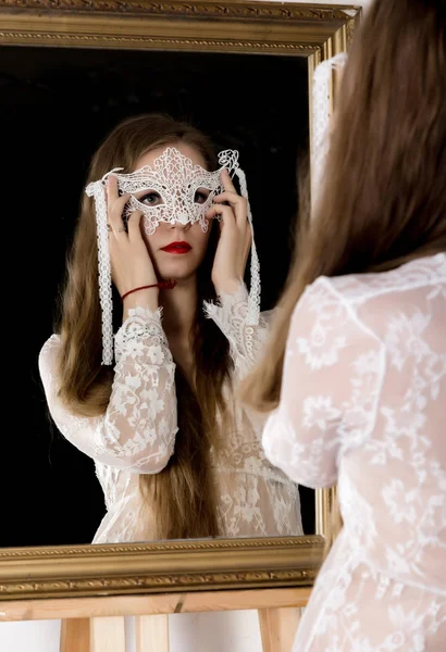Belleza mujer joven sosteniendo una máscara de encaje y se mira en el espejo como su retrato — Foto de Stock