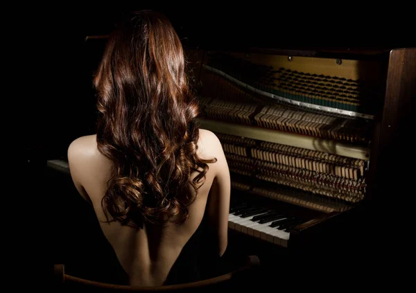 Bella giovane donna in abito nero con la schiena aperta seduta nere il pianoforte su uno sfondo scuro — Foto Stock