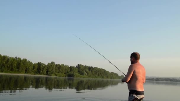 Rybář loví v klidné řeky ráno. Muž v stending gear rybaření v řece a vyvolá rybářský prut — Stock video