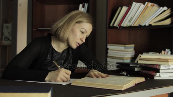 Жіночий викладач, що працює з книжками в бібліотеці в коледжі. втомлений студент готується до іспитів — стокове відео