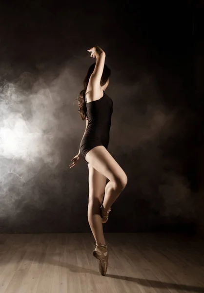 Jovem bela dançarina de balé em sapatos pontiagudos, dançando em uma fumaça em um fundo escuro . — Fotografia de Stock
