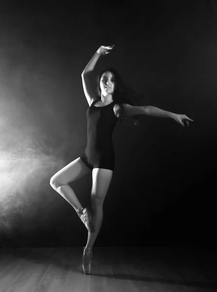 Jovem bela dançarina de balé em sapatos pontiagudos, dançando em uma fumaça em um fundo escuro. preto e branco — Fotografia de Stock