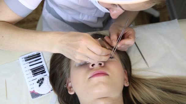 Beautician increases eyelashes for beautiful girl. Eyelash extension procedure — Stock Video