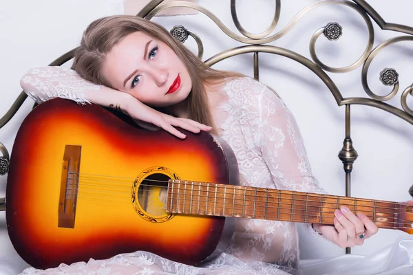 Bela jovem tocando música em uma cama com felicidade e guitarra — Fotografia de Stock