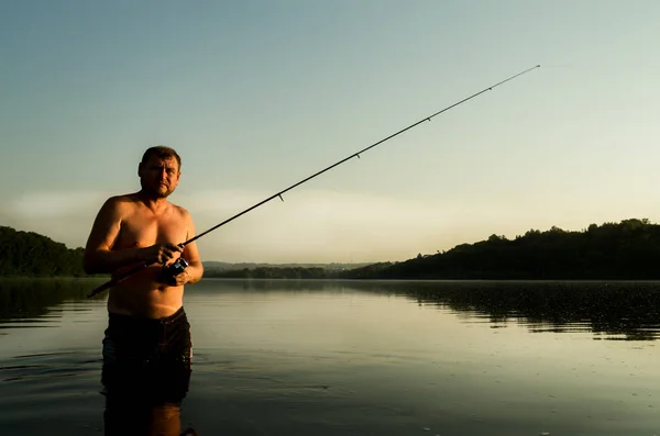 Pescador pesca em um rio calmo na parte da manhã. Homem em artes de pesca que se encaixa em um rio e joga um pólo de pesca — Fotografia de Stock