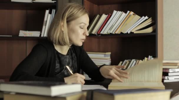 Joven mujer Ph.D. se está preparando para una conferencia, sentado en el escritorio y escribe la información necesaria del libro — Vídeo de stock