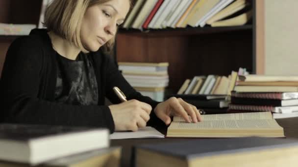 Jonge vrouwelijke graduate bereidt zich voor een lezing, zitten aan de balie en schrijft uit de nodige informatie uit het boek — Stockvideo