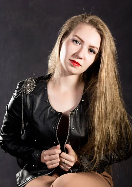 Bela jovem mulher em uma jaqueta de couro posando em um fundo cinza — Fotografia de Stock