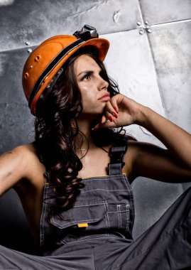 Turuncu kask çelik arka plan üzerinde bir katta oturan el feneri ile güzel yorgun seksi madenci işçi