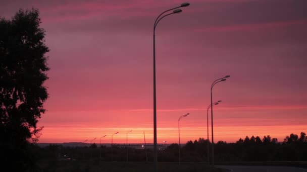 Brillante sol naranja-rojo se levanta sobre la carretera, líneas de transmisión eléctrica, edificios y árboles . — Vídeos de Stock