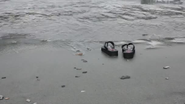 Flip Flops am grau-gelben Sandstrand in der Nähe von Meereswellen. Urlaubskonzept — Stockvideo