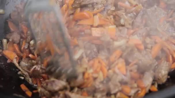 Приготовление плова с ягненком, морковью и луком в котле на дровяной печи — стоковое видео
