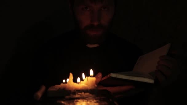 Prêtre allume des bougies et la lecture de la Sainte Bible dans un noir — Video