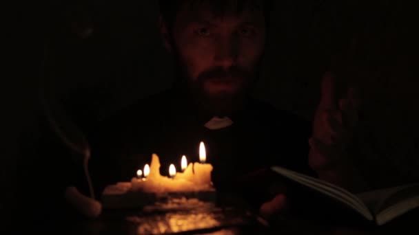 Священик запалює свічки і читає зі Святої Біблії в темряві — стокове відео