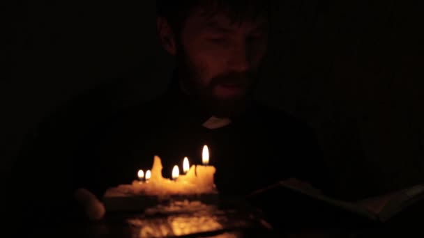 Pasteur catholique allume des bougies et la lecture de la Sainte Bible dans un noir — Video