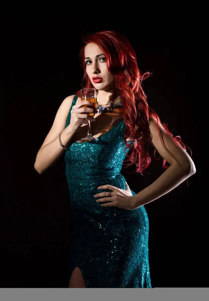Giovane rossa donna sexy in abito elegante blu in possesso di bicchieri da vino con champagne e posa in un buio . — Foto Stock