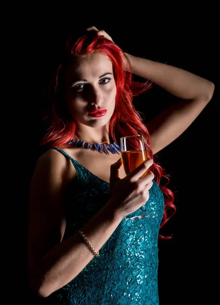 Giovane rossa donna sexy in abito elegante blu in possesso di bicchieri da vino con champagne e posa in un buio . — Foto Stock