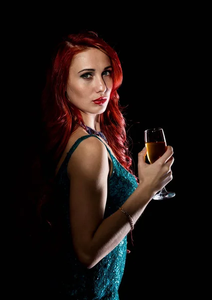 Sexy kobieta młoda rude w niebieska sukienka trzyma kieliszek z szampanem i pozach w ciemności. — Zdjęcie stockowe