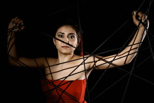 Bela jovem mulher em vestido vermelho emaranhado em uma teia de aranha de corda em um fundo preto — Fotografia de Stock