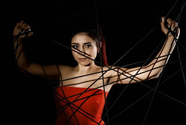 Красивая молодая женщина в красном платье запуталась в веревке паутины на черном фоне — стоковое фото