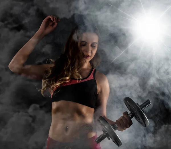 Gimnasio joven en el entrenamiento con pesas, deportivo musculoso morena femenina en el humo — Foto de Stock
