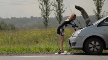 sarışın kız kırık arabası ile açık bir ülke yolunda kaputa yakınındaki bir panik içinde cep telefonu arama
