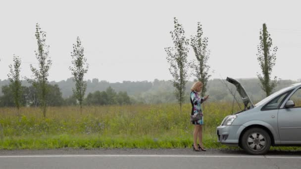 Schönes Mädchen telefoniert mit Handy in der Nähe ihres kaputten Autos auf einer Landstraße — Stockvideo