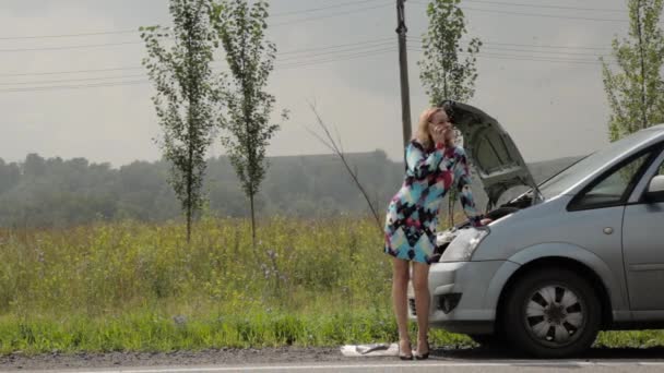 Chica rubia llamando al teléfono celular en un pánico cerca de su coche roto con capucha abierta en una carretera de campo — Vídeos de Stock