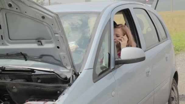 Блондинка звонит на мобильный в панике сидя в разбитой машине с открытым капюшоном на проселочной дороге — стоковое видео