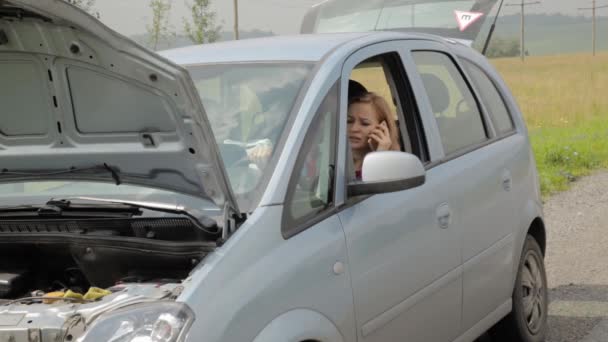 Chica rubia llamando al teléfono celular en un pánico sentado en su coche roto con capucha abierta en una carretera de campo — Vídeos de Stock