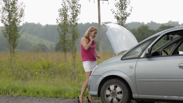 Blond flicka ringer mobiltelefon i panik nära hennes trasiga bil med öppen huv på en landsväg — Stockvideo