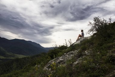 Dağın tepesinde oturan ve gökyüzü bulutlar düşünürken güzel kadın