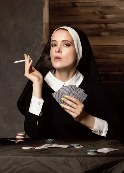 Hermosa monja católica fuma y juega a las cartas. Religión podrida — Foto de Stock