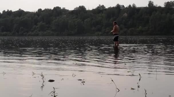 Pescatore mezzo nudo con una canna da pesca pesca nel fiume calmo — Video Stock