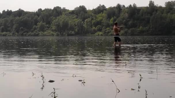 Pescatore mezzo nudo con una canna da pesca pesca nel fiume calmo — Video Stock