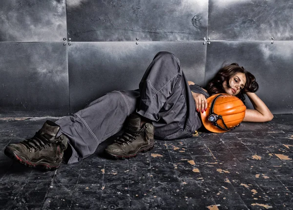 Krásné sexy unavený horník dělník v oranžovou helmu s baterkou leží na podlaze na ocelové pozadí — Stock fotografie