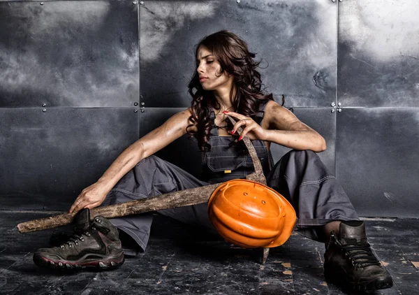 Beautiful tired sexy miner worker in orange helmet with flashlight sitting on a floor on steel background. woman holding pickaxe