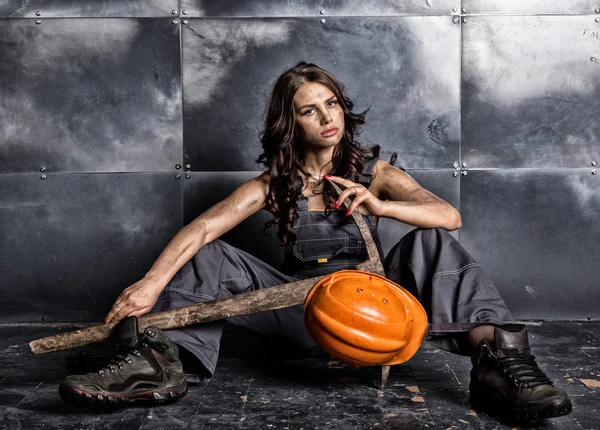 Belo trabalhador mineiro sexy cansado em capacete laranja com lanterna sentada em um piso em fundo de aço. mulher segurando picareta — Fotografia de Stock