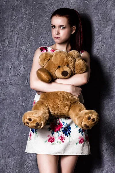 Nachdenkliche oder beleidigte schöne Frau umarmt einen Teddybär auf grauem Hintergrund. — Stockfoto