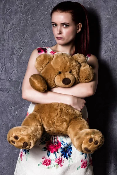 Mujer hermosa pensativo u ofendido abraza un oso de peluche sobre un fondo gris . — Foto de Stock