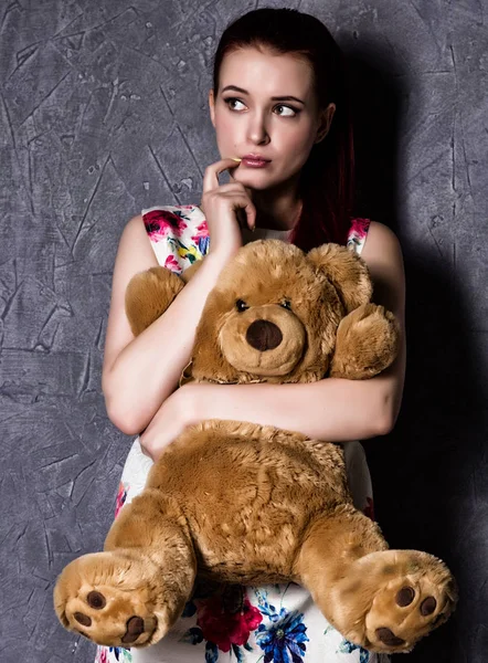 Mujer hermosa pensativo u ofendido abraza un oso de peluche sobre un fondo gris . — Foto de Stock