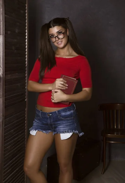Hermosa estudiante con libro. mujer joven en top rojo y pantalones cortos de mezclilla con gafas — Foto de Stock