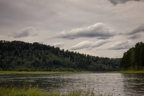 Landschaft mit Fluss, Bergen und Wald an einem Ufer. Himmel mit Gewitterwolken über dem Fluss — Stockfoto