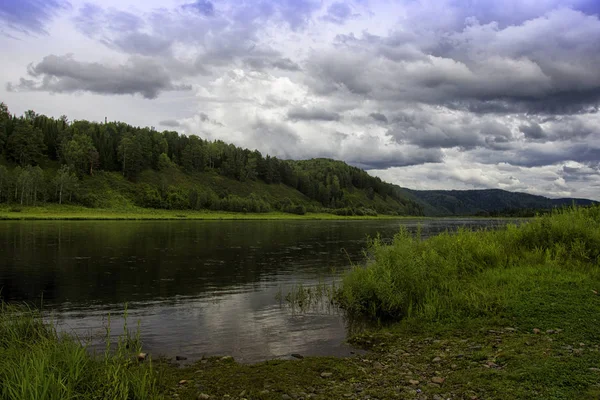 Landschaft mit Fluss, Bergen und Wald an einem Ufer. Himmel mit Gewitterwolken über dem Fluss — Stockfoto
