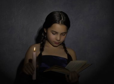 kitap okuma ve mum ışık karanlık odada okuyan küçük kız