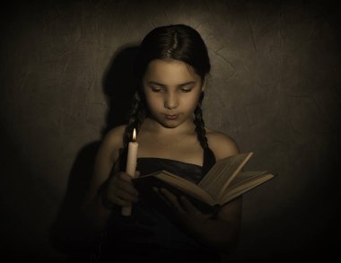 kitap okuma ve mum ışık karanlık odada okuyan küçük kız