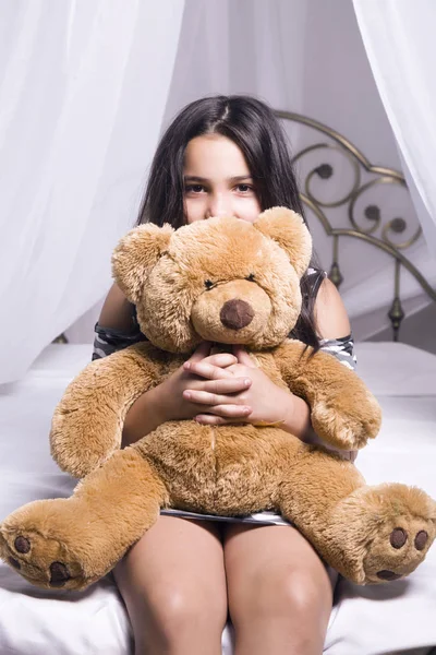 Gülümseyen kız yatağında evde oturan bir oyuncak ayı sarılma