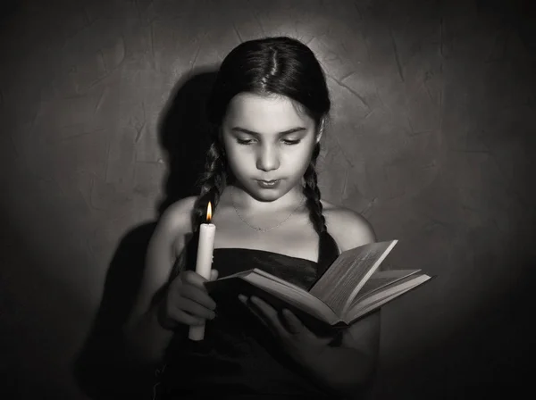 Μικρό κορίτσι ανάγνωση του βιβλίου και μελετώντας το φως κεριών σε σκοτεινό δωμάτιο — Φωτογραφία Αρχείου