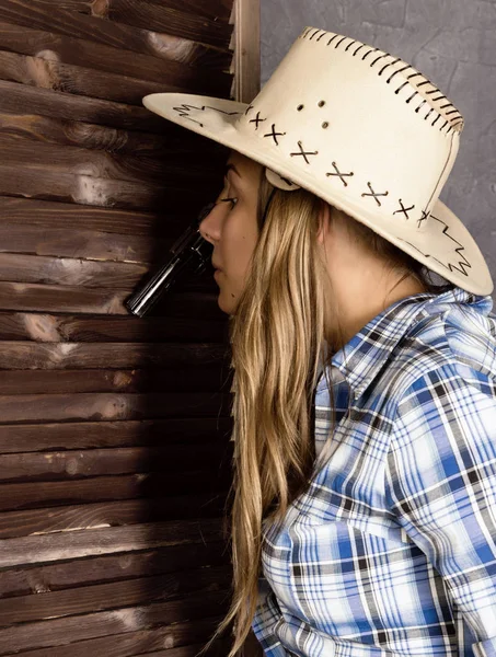 cowboy girl or pretty woman in stylish hat and blue plaid shirt holding gun and old suitcase