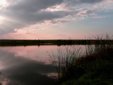 Göl, thunderclouds ve çim bir kıyısında günbatımı